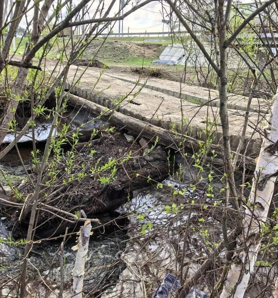 После схода льда и снега основание моста просело: одна плита треснула, часть конструкции накренилась. Местные засыпали дыру камнями и боятся, что переправа обрушится, спецтехника не проезжает.