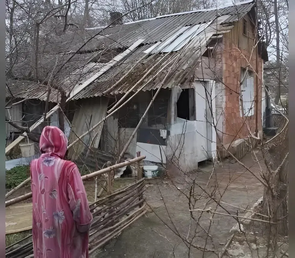 Жительница Балткоса уже более десяти лет живёт в здании, снятом с баланса: отопление дровяное, нет водоснабжения и канализации. После недавнего шторма крыша повреждена, соседи пытаются помочь, женщина отказывается от переезда в дом престарелых.