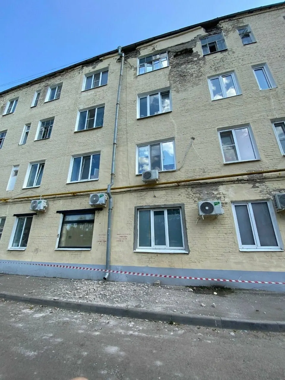 С кусков фасада одного из домов сыплется бетон. УК ограничила проход лентой — в ливень единственный сухой путь проходит прямо под падающими фрагментами, остальные дорожки затоплены до щиколотки.