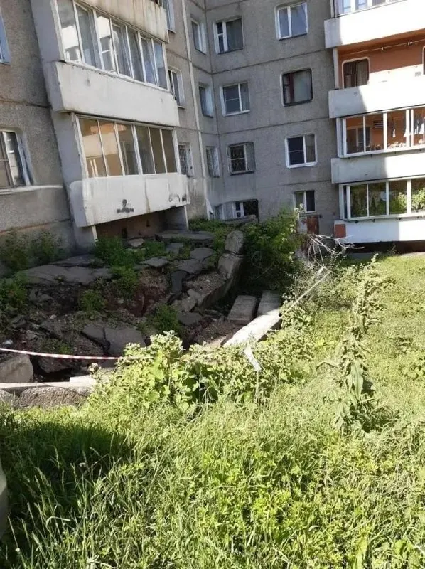 В микрорайоне Радужный под балконами девятиэтажного дома образовался глубокий провал: бетонные плиты ушли под землю, опасный участок огородили только лентой, рядом — детская площадка. Жильцы жалуются, что управляющая компания не начала ремонт.