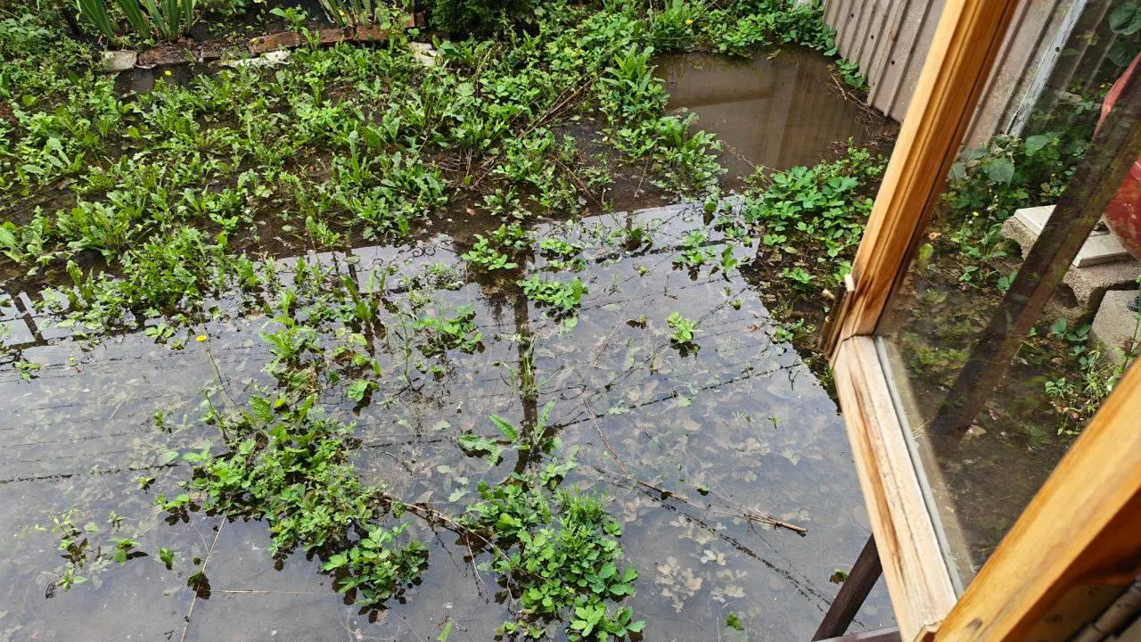 После прорыва трубы холодного водоснабжения на улице Металлистов вода заливает дворы, опора линии электропередач наклоняется — растёт риск повреждения домов. Жители пытаются откачать воду и ждут устранения течи.