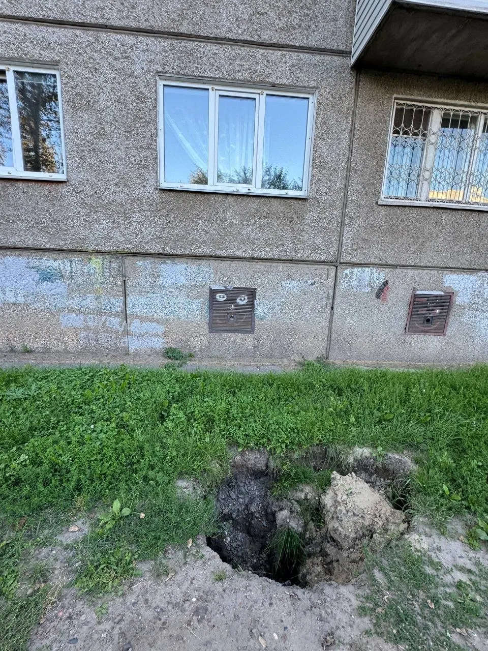 Грунтовые провалы в проходе между домом и детским садом угрожают пешеходам и основам зданий; жители просят ограждения, засыпку и обследование подземных сетей.