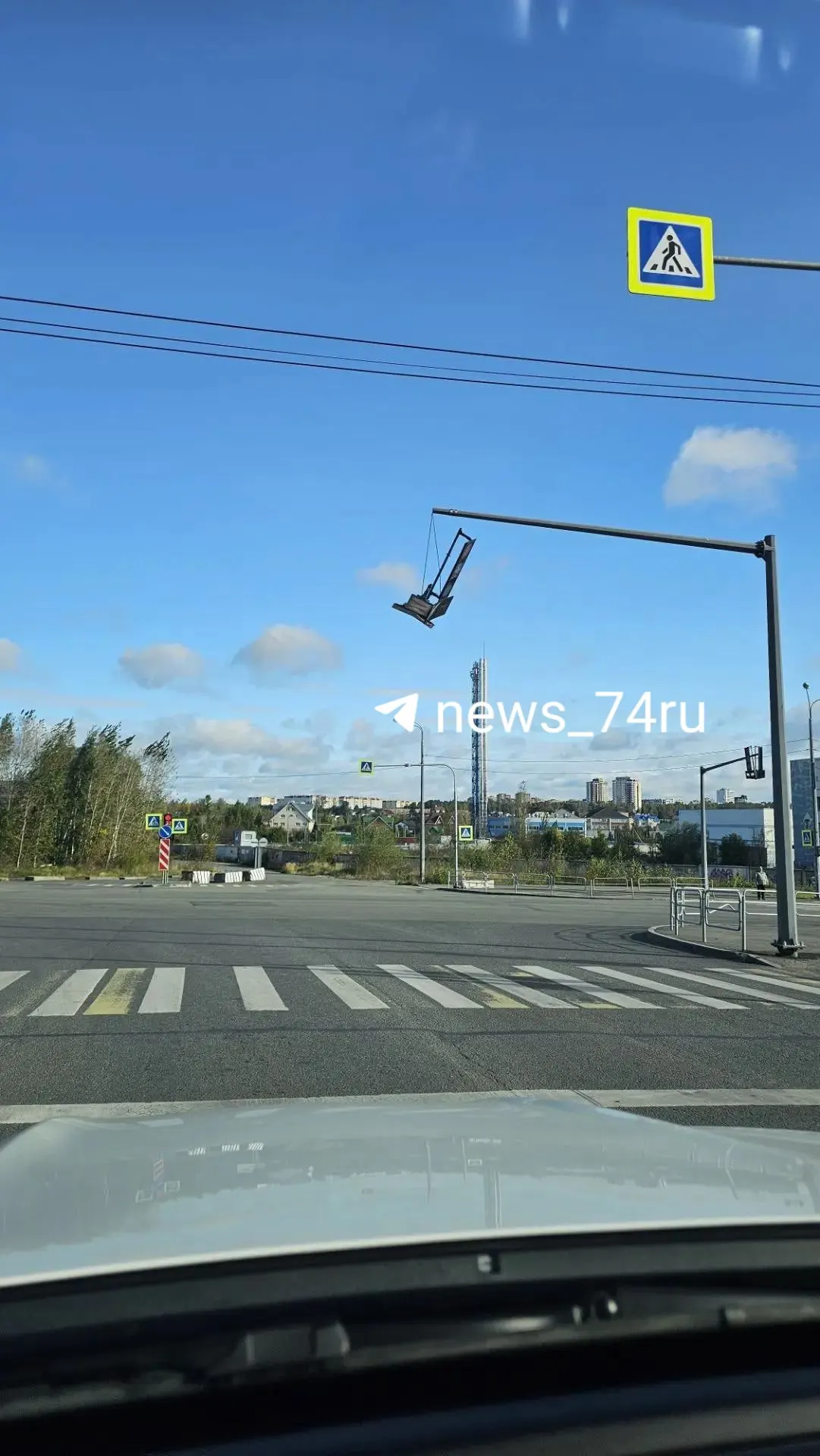 На перекрестке над переходом заметен подвешенный светофор; пешеходам рекомендуется внимательно смотреть вверх и двигаться осторожно.