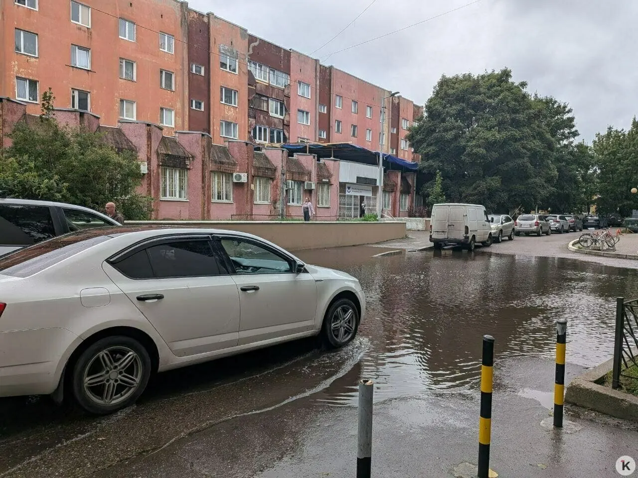 У входа в поликлинику образовалась массивная лужа после недавнего ливня, проход к дверям затруднен; жители ищут обходы по газону и забору. Власти обещали разобраться с ливневкой.
